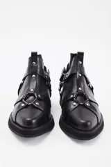 Botineta de cuero vacuno color negro, con diseño estilo western que incluye tiras decorativas, argollas metálicas y tachas plateadas. Cuenta con suela de goma y taco bajo cuadrado.