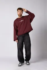 Buzo de cuello redondo confeccionado en tejido rústico con bordes al corte y costuras expuestas. Presenta un diseño boxy con estampado frontal y es reversible, permitiendo su uso por ambos lados.