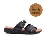 Sandalias bajas de cuero negro, con dos tiras anchas sobre el empeine, una con hebilla dorada ajustable y otra cruzada. Plantilla acolchada color suela y suela de goma negra con tecnología Low Impact para absorción de impactos.