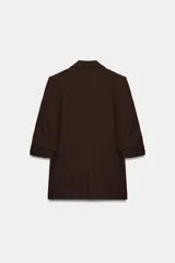 Blazer negro con cuello solapa con muescas, hombreras y forro interior a tono. Presenta manga por debajo del codo con detalle de drapeado y falsos bolsillos de vivo en el delantero, con cierre frontal de un solo botón dorado.