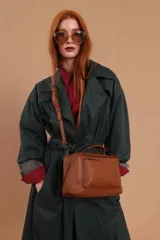 Bandolera de diseño rectangular en color suela, confeccionada en material sintético. Cuenta con un asa superior fija, correa larga ajustable y extraíble, y dos bolsillos frontales con cierre metálico, uno de ellos con diseño superpuesto. Presenta el logo de la marca grabado en el frente.