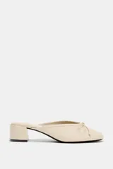 Zapatos de tacón tipo bailarina destalonada en piel color beige, con detalle de lazo en la parte delantera, tacón en bloque y punta redonda.