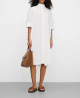 Vestido camisero midi blanco de algodón orgánico, con cuello tipo tira, mangas raglán sobre el codo, botonadura frontal oculta y canesú con pliegues en la espalda.