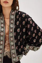 Kimono corto de estilo bohemio, confeccionado en viscosa negra con estampado paisley y detalles bordados en los bordes frontales y mangas. Presenta mangas tres cuartos y un lazo ajustable en la cintura con estampado animal print.