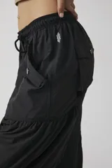 Pantalón jogger negro de inspiración utility, confeccionado en tejido liviano de poliamida. Cuenta con cintura elástica ajustable con cordón, bolsillos cargo con broches metálicos, diseño con paneles fruncidos y puños elastizados.