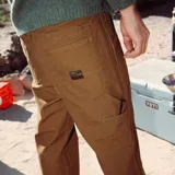 Pantalón de trabajo estilo cargo color marrón, confeccionado en resistente tela de algodón. Presenta un diseño de cinco bolsillos, incluyendo compartimentos utilitarios, cierre frontal con botón y trabillas reforzadas para cinturón.