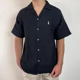 Camisa de hombre color verde oliva, de muselina con textura arrugada, manga corta, corte oversize, cuello cubano y cierre con botones. Presenta un pequeño logo bordado en el pecho.