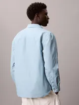 Sobrecamisa de algodón de corte regular, color celeste, con cierre frontal de botones a presión, bolsillos frontales con solapa y puños abotonados. Presenta un parche con el logo de la marca en el bolsillo superior izquierdo.