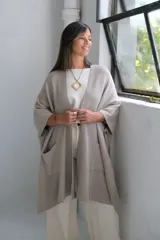 Poncho abierto de tejido de punto en color visón, con diseño holgado, mangas cortas y bolsillos frontales aplicados.