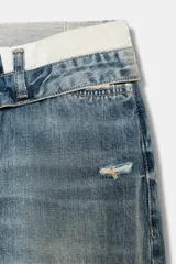 Jeans de tiro medio con diseño de cintura doblada, cinco bolsillos y cierre frontal con cremallera y botón metálico. Presenta un acabado desgastado con roturas en las rodillas y corte recto.