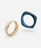 Kit de dos brazaletes, uno rígido de resina en color azul traslúcido con forma orgánica y otro de metal liso en tono dorado con diseño redondeado.
