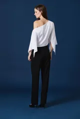 Blusa blanca de un solo hombro con mangas amplias y fluidas. Presenta un diseño asimétrico con un broche decorativo en forma de libélula en el hombro derecho.