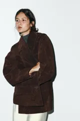 Chaqueta tipo blazer oversize de piel de ante color marrón oscuro, con cuello solapa de muescas, manga larga y bolsillos delanteros con solapa. Cierre frontal con botones.