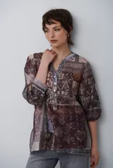 Camisa de corte holgado con estampado tipo patchwork en tonos marrones y beige. Presenta cuello redondo con escote en V, cierre frontal parcial con botones y mangas tres cuartos con puños elásticos.