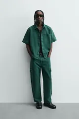 Camisa de denim de algodón color verde oscuro, de corte relajado (relaxed fit) y manga corta. Posee cuello solapa, bolsillo plastrón en el pecho con bordado a tono y cierre frontal de botones.