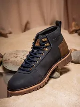 Botines de cuero color azul marino con detalles en cuero marrón en el talón. Presentan un diseño inspirado en Star Wars con el logo grabado en el talón y el Halcón Milenario en el lateral. Cuentan con cordones oscuros, ojales metálicos dorados y una suela robusta de goma en tono tierra.