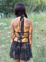 Vestido corto color chocolate con cuello halter y escote drapeado. Presenta un diseño con falda fluida y short incorporado, confeccionado en tela liviana y traslúcida.