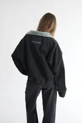 Campera bomber de denim azul oscuro con costuras a contratono en color verde. Presenta cuello de corderito en color marrón, cierre frontal y diseño holgado.