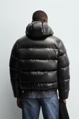 Campera puffer negra con capucha, cierre frontal con cremallera, bolsillos laterales con cremallera y puños elásticos.