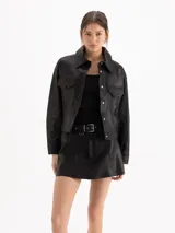 Chaqueta de cuero ovino color negro, con textura graneada, silueta de hombros caídos y largo a la cadera. Presenta recortes en el delantero y la espalda, dos bolsillos superiores con tapa y dos bolsillos laterales, cierre frontal con botones metálicos y cuello camisero.