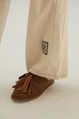 Pantalón de corte recto y tiro medio con costuras a la vista, bolsillos delanteros y traseros, y un detalle de pin de la marca en el ruedo.