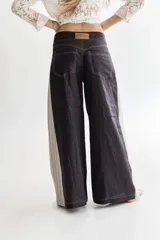 Pantalón de lino negro, de piernas anchas con cadera al cuerpo y cintura media. Tiene apliques triangulares de lino rayado en los costados.
