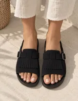 Sandalia negra de diseño destalonado con capellada ancha, detalle de flecos y tira con hebilla ajustable metálica.