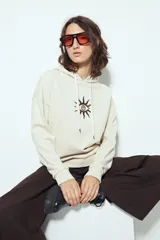 Canguro negro de calce relajado con capucha y cordones ajustables. Presenta un estampado gráfico frontal de un ojo con rayos de sol y la frase "STAY WEIRD".