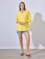 Blusa amarilla de tejido acanalado con cuello redondo, escote en V y aplique metálico. Manga ¾.