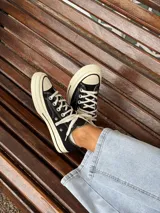 Zapatillas bajas de lona color blanco, con cordones marrones, puntera de goma y base blanca.