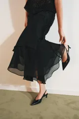 Falda midi negra de tiro medio con superposición de tejido transparente con diseño estampado y aplicación de abalorios a tono. Presenta bajo asimétrico con volantes y forro interior negro.