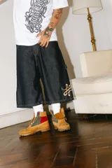 Bermuda de jean color azul oscuro (raw), corte baggy carpintero, con grandes bolsillos frontales y traseros. Presenta un bordado dorado con un monograma en la parte inferior lateral derecha.