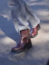 Botas de cuero marrón con suela track de goma negra, cierre lateral en color rojo y detalle de tira trasera al tono.