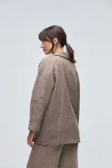 Chaquetón de lana fina sin teñir, con cuello camisero, cierre frontal de botones y bolsillos delanteros. Diseño de corte recto y estructura clásica.