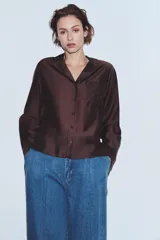 Camisa de manga larga color marrón oscuro, con cuello solapa, escote pico y bajo asimétrico. Presenta un bolsillo plastrón en el delantero con bordado combinado a tono.