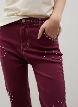 Pantalón de denim negro con diseño de tachas metálicas distribuidas en patrones curvos. Presenta un corte recto y tiro medio.