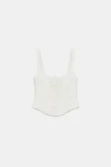 Top estilo corset de color blanco con escote cuadrado y tirantes anchos. Presenta paneles laterales y centrales con tejido drapeado, estructura entallada y cierre posterior con cremallera.
