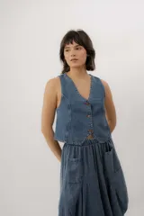Chaleco de denim azul con cuello en V, cierre frontal con botones metálicos y pespuntes en contraste.