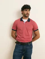 Remera polo rosada con cuello y ribetes de las mangas en azul marino, bolsillo ojal en el pecho y cierre frontal parcial con botones.