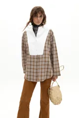 Camisa de corte oversized confeccionada en popelina de algodón con estampado de cuadros en tonos marrones y blancos. Presenta cuello mao, mangas largas y una pechera blanca en contraste que le otorga un estilo sastrero y descontracturado.