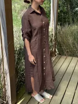 Vestido camisero largo de lino blanco, con cuello camisero, manga corta enrollada y cierre frontal de botones de nácar. Presenta aberturas laterales en el bajo.