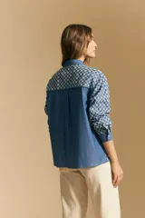 Camisa de manga larga, color azul, con cuello camisero y estampado geométrico en blanco. Presenta un diseño de doble capa: una camisa exterior abierta con botones y un top anudado debajo.