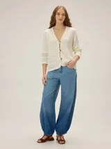 Cardigan de punto color blanco marfil, con escote en V, mangas largas con detalles de tejido calado y cierre frontal de botones con efecto madera.