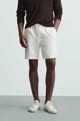 Bermuda negra de corte recto, con cintura elástica ajustable mediante cordón, pliegues frontales y bolsillos de vivo en la espalda. El bajo tiene un dobladillo vuelto.