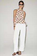 Top beige con estampado de lunares bordó, cuello halter, diseño sin mangas y bajo con volantes. Cuenta con cierre de lazada en la espalda.