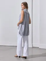 Camisa sin mangas de corte recto, con cuello clásico y escote en V. Presenta un diseño de rayas verticales en tonos lila, rosa, blanco y gris, con dos bolsillos frontales aplicados con estampado en chevron. Cuenta con cierre central de botones.