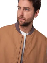 Chaleco de trabajo Caterpillar, color marrón, con cierre frontal, cuello tipo bomber y bolsillos laterales. Presenta parche de la marca en el pecho y forro interno.
