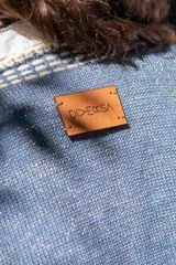 Chaleco tejido de punto color azul con destellos de lurex, escote en V y cierre frontal con botones. Presenta detalles de bordado artesanal en lana blanca en los bordes y terminaciones en crochet.