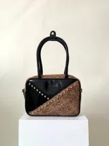 Cartera rígida negra con detalles en rojo y tachas plateadas. Tiene herrajes y cierre metálico plateado marca YKK, asa fina para llevar al hombro o en la mano y correa larga extra regulable. El interior es forrado, tiene un bolsillo con cierre enmarcado en cuero, y un segundo bolsillo plaqué.