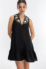 Vestido corto negro de lino con cuello mao y escote en V. Presenta apliques metálicos dorados en los hombros y ruedo con volantes.
